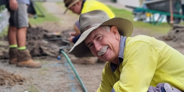 Male landscaper tending to irrigation pipe kneeling down and smiling